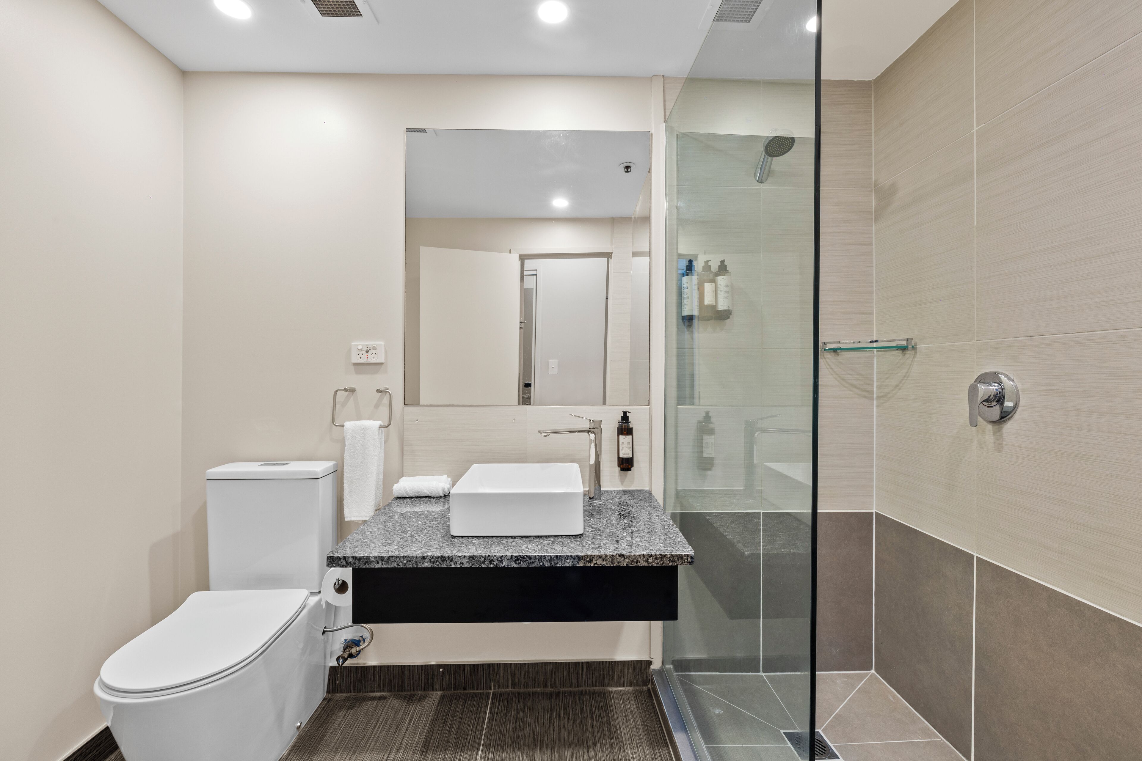Une salle de bain moderne avec une douche à parois de verre, des toilettes blanches et un lavabo sur un plan de travail en granit.