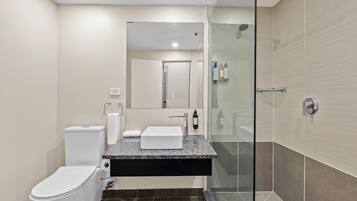 Une salle de bain moderne avec une douche à parois de verre, des toilettes blanches et un lavabo sur un plan de travail en granit.