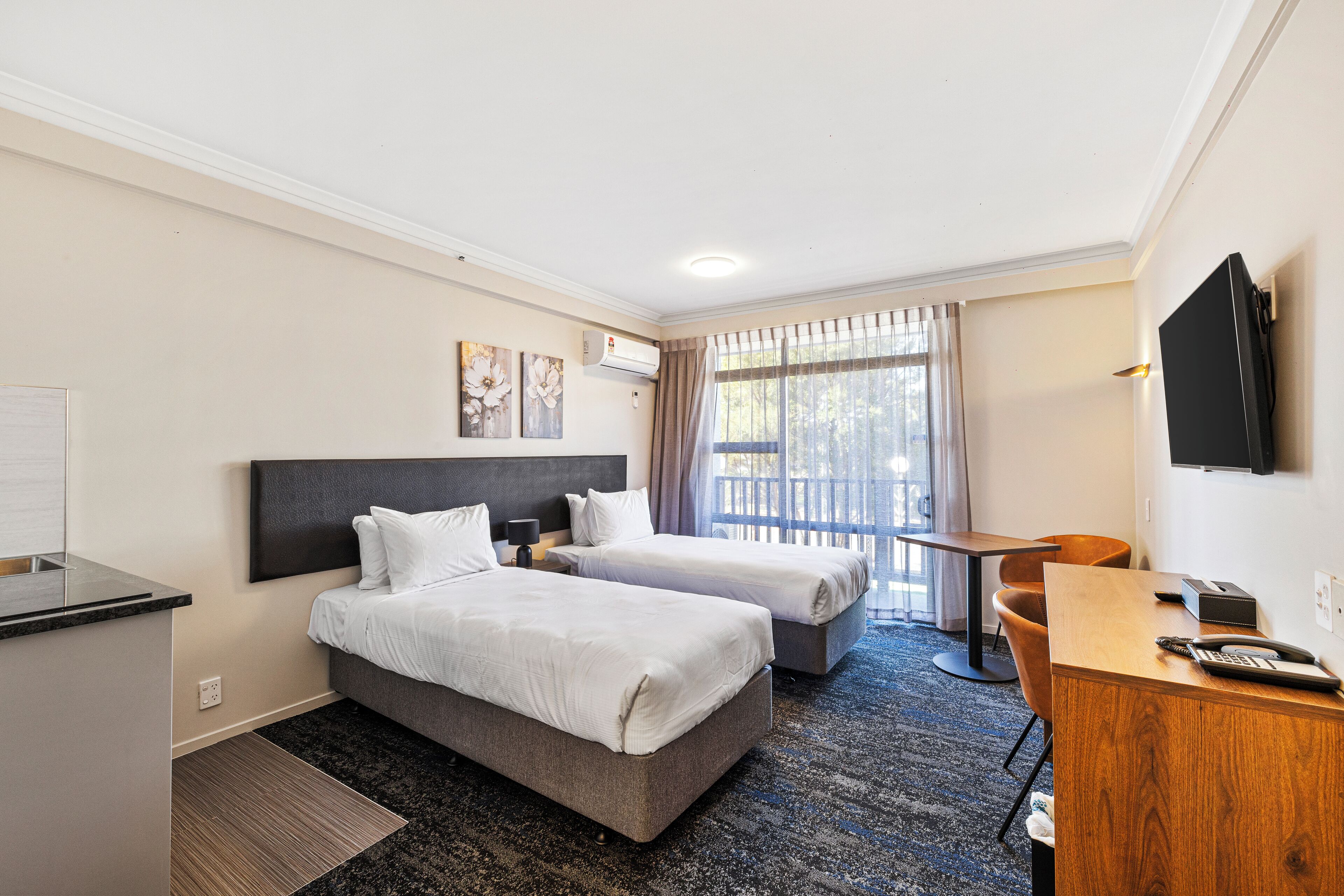 Quarto de hotel com duas camas, uma mesa, uma televisão e uma janela com cortinas.