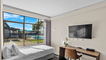 A hotel room with a bed, a desk, a chair, a TV, and a view of a swimming pool.