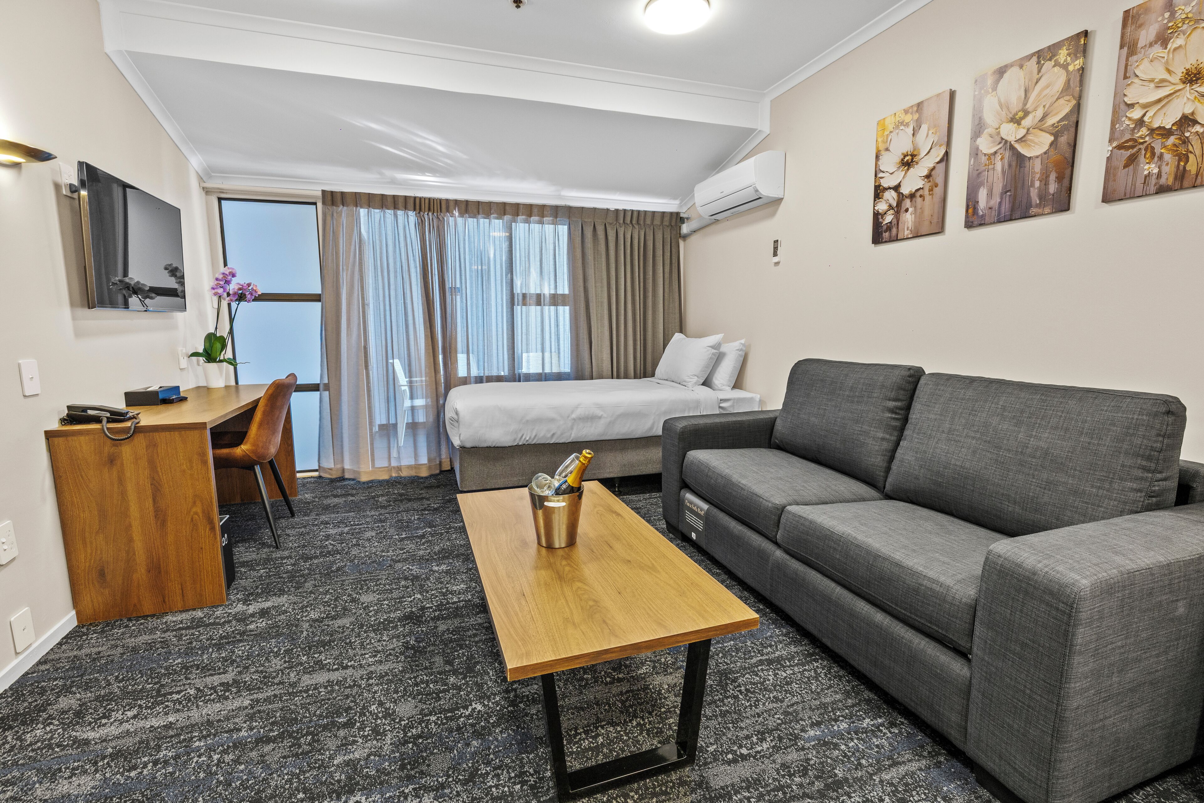 Una habitación de hotel moderna con una cama, un sofá gris, un escritorio de madera y una mesita.