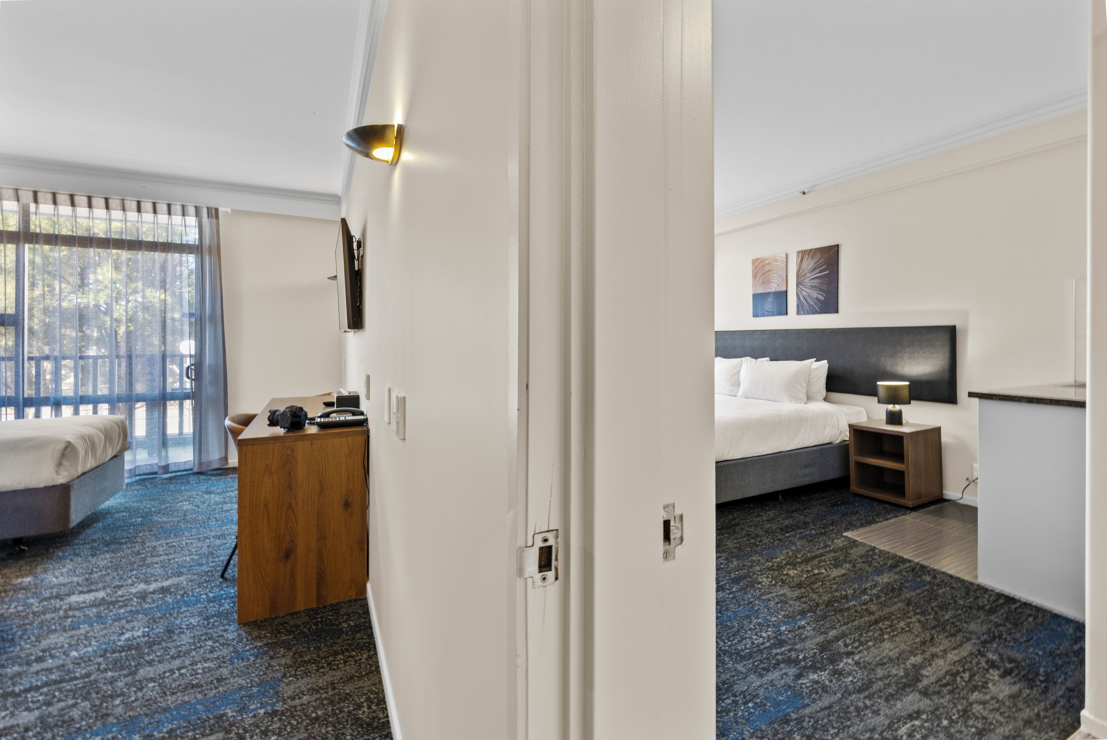 A hotel room with a bed, a desk, a chair, a nightstand, and a window with blinds.