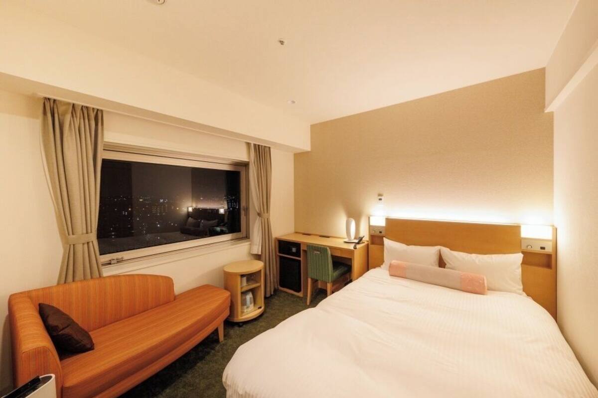 A hotel room with a bed, a sofa, a desk, and a window with curtains.