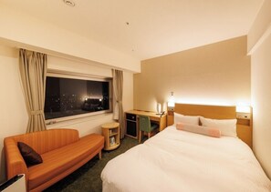 Una habitación de hotel con cama, sofá, escritorio y ventana con cortinas.