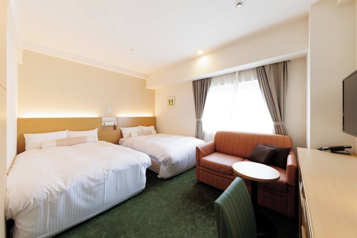 A hotel room with two beds, a sofa, a small table, and a TV.