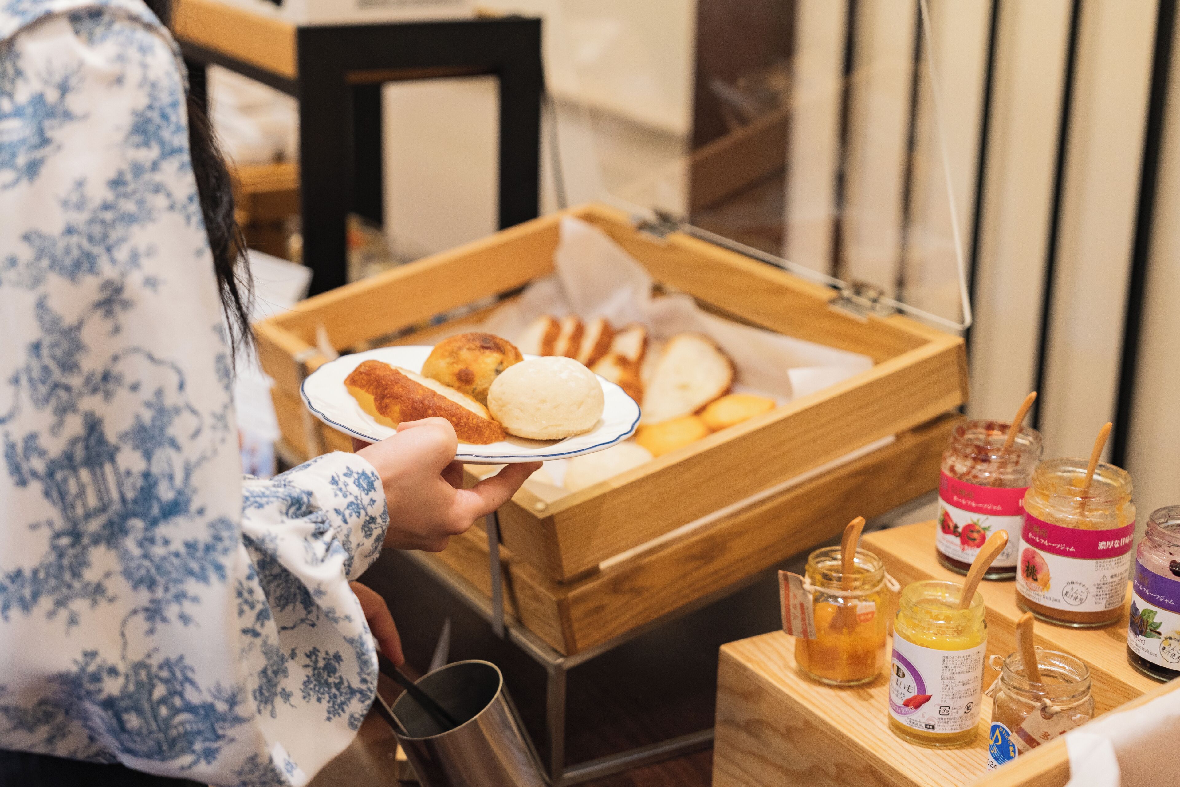 Une personne tenant une assiette remplie de différents aliments, un plateau en bois contenant d’autres plats et des pots de condiments placés sur une table.