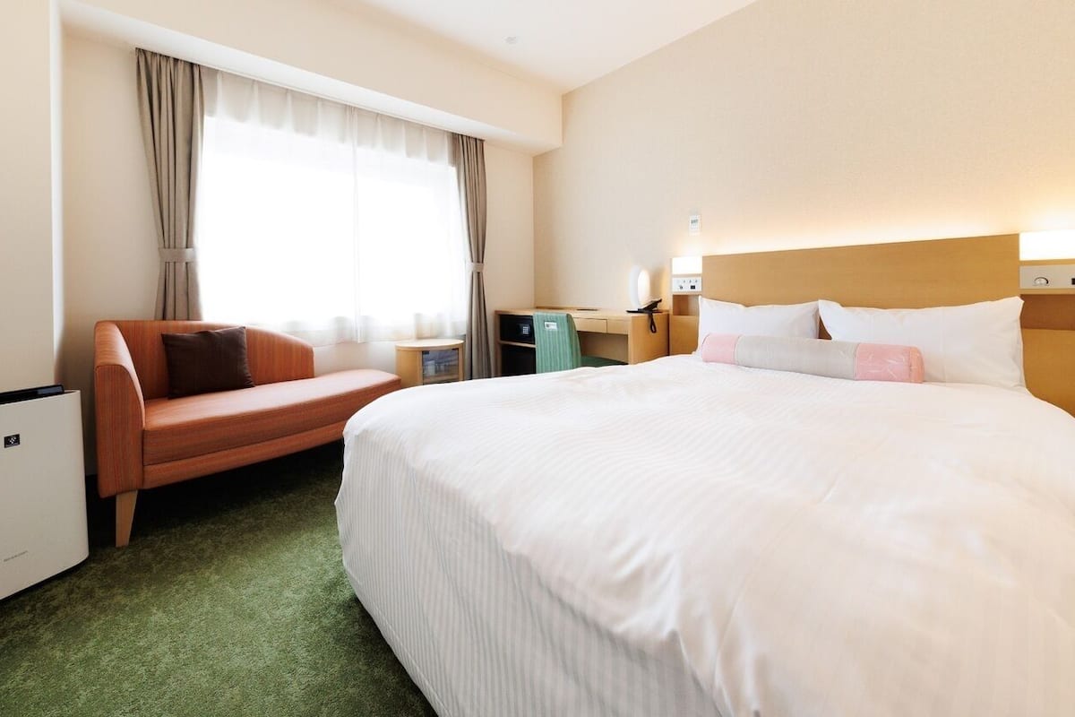 A hotel room with a bed, a sofa, a desk, and a small refrigerator.