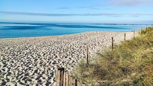Une plage de sable avec une clôture en bois et de l’herbe sur le côté droit.