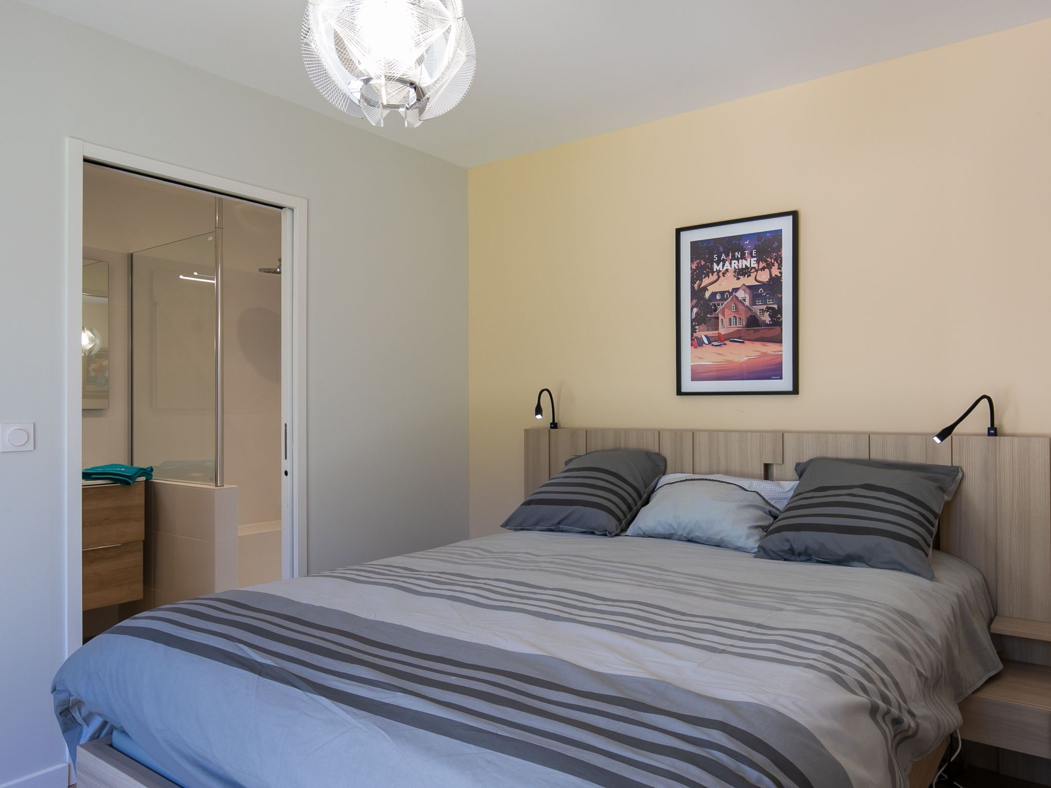 Een slaapkamer met een bed, nachtkastje, een lijst met een afbeelding en een deur naar een badkamer.
