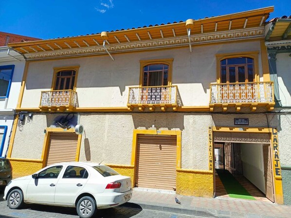 A two-story building with a yellow facade, balconies with white railings, and a closed shuttered entrance. - El Renacimiento (Cuenca)