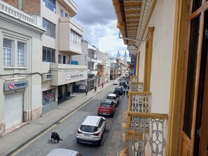 A narrow street lined with buildings, some with balconies and storefronts, under a cloudy sky. - El Renacimiento (Cuenca)