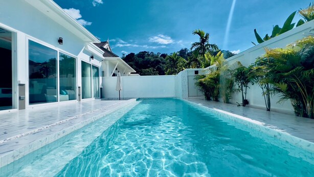 A modern pool area with clear blue water, surrounded by a white building with large glass doors and a tiled deck. - Kamala Garden View Villas by Aladdin (Kamala)
