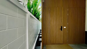 A hallway with a white brick wall, a wooden door, and a small mat at the entrance. - Kamala Garden View Villas by Aladdin (Kamala)