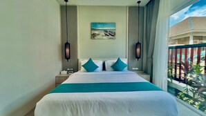 A hotel room with a large bed, two nightstands, a painting of a beach scene, and a balcony with plants. - Kamala Garden View Villas by Aladdin (Kamala)