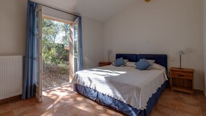 Ein Schlafzimmer mit einem Bett, zwei Nachttischen, einem Fenster mit Vorhängen und Blick ins Grüne.