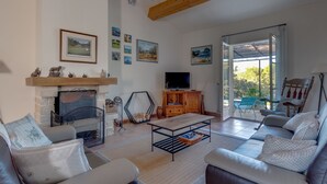 Ein Wohnzimmer mit Kamin, Sofa, Fernseher und Blick durch eine Glastür.