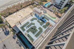 An aerial view of a rooftop with a pool, a tennis court, and a small building. - Updated & Oceanfront 3BR W/ Waterpark & Views! (Myrtle Beach)
