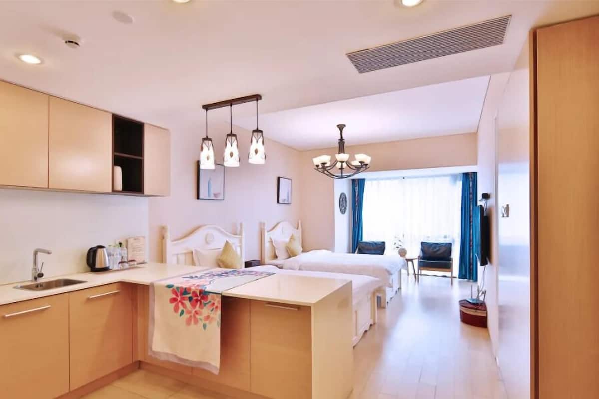 A modern hotel room with a kitchenette, a large bed, a sitting area, and a view of the outdoors.