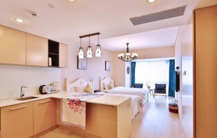 A modern hotel room with a kitchenette, a large bed, a sitting area, and a view of the outdoors.