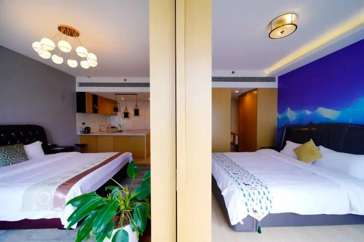 Two hotel rooms with modern decor, including a bed with a white bedspread and a headboard, a bedside table, and a large potted plant.