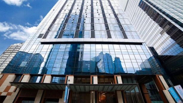 Un immeuble moderne de grande hauteur, doté de fenêtres en verre réfléchissant et d’un hall d’entrée imposant.