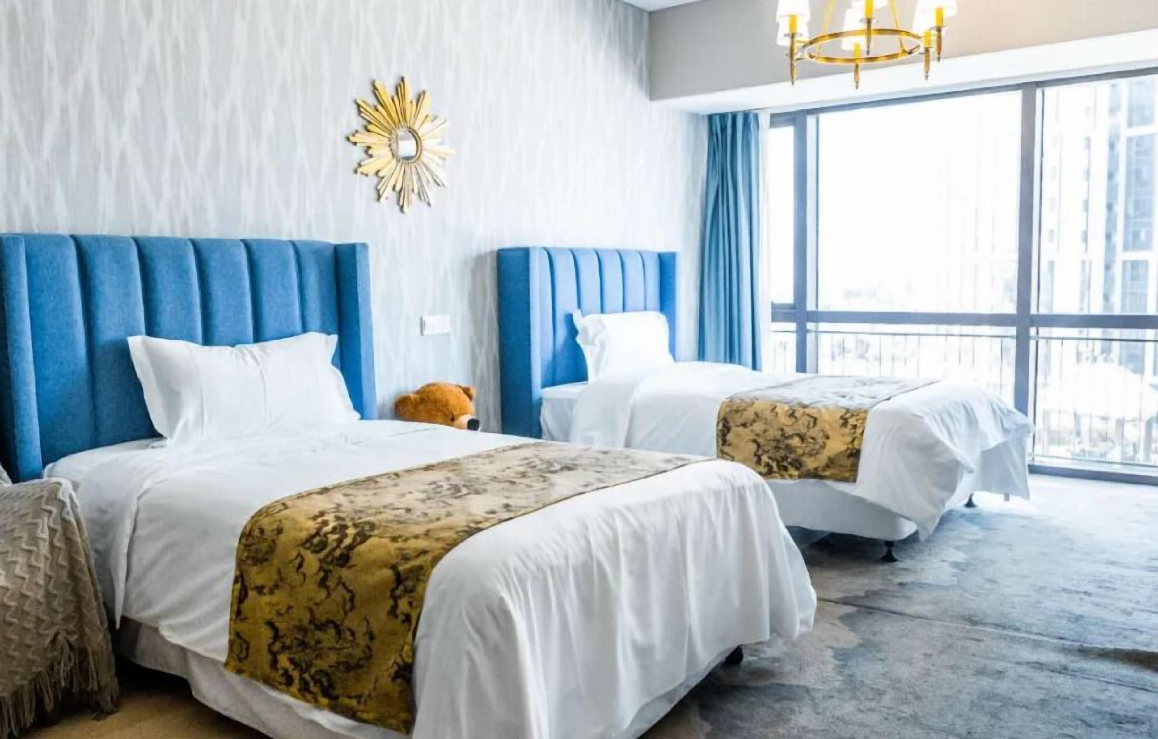 A hotel room with two beds, a large window, and a chandelier.