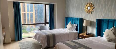 A hotel room with two beds, a large window with curtains, a modern chandelier, and a decorative wall piece.