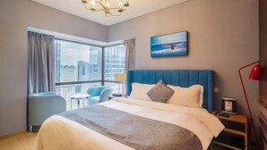 Une chambre d’hôtel avec un grand lit, une vue sur la ville, un fauteuil bleu et un lustre.