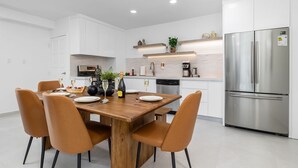 A modern kitchen with white cabinets, a stainless steel refrigerator, and a wooden dining table with chairs.