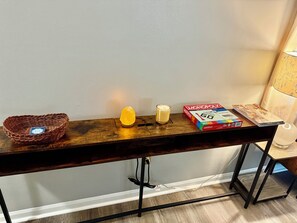 A wooden table with a woven basket, a candle, a Monopoly game box, and a lamp.