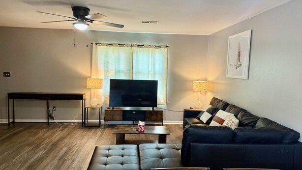 A living room with a sofa, a television, two lamps, a ceiling fan, and a window with curtains. - 3-bedroom townhouse - Max 8 guests (Charlotte)