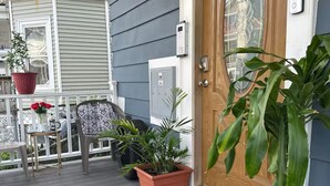 Una puerta de madera con felpudo, plantas en macetas y un porche con mesa y sillas.