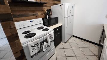 A kitchen with a white stove, a microwave, and a refrigerator. There is a wooden wall panel and a shelf above the stove.