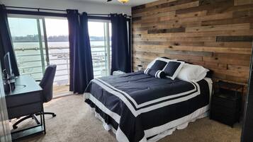 Een slaapkamer met een groot bed, een bureau en uitzicht op een waterlichaam.