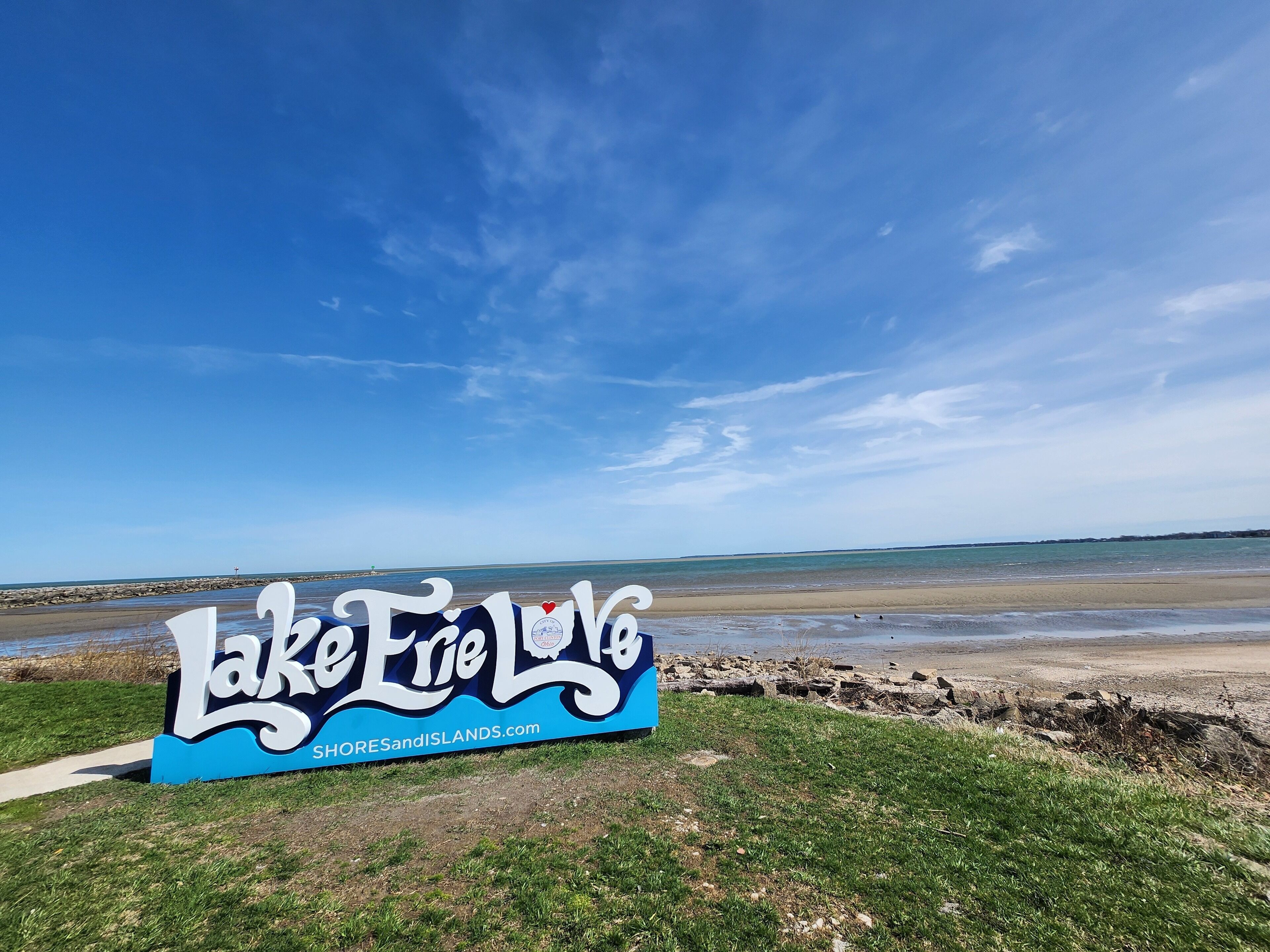 A sign for Lake Erie Shores and Islands with a clear sky and beach in the background.
