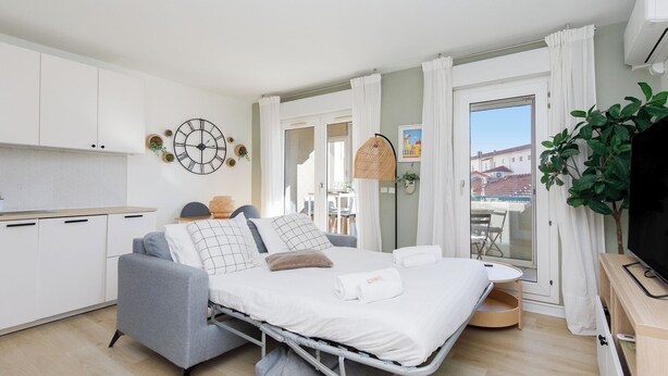 Een compacte hotelkamer met een bed, een kitchenette, een balkon met uitzicht en een televisie.