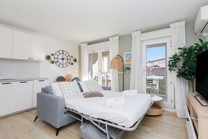 Ein kompaktes Hotelzimmer mit Bett, Küchenzeile, Balkon und Fernseher.