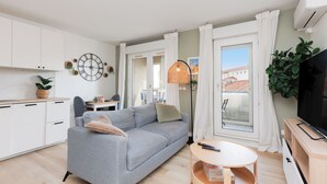 Een modern appartement met een grijze bank, een eettafel, een televisie en een balkon met uitzicht.