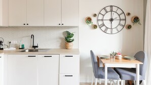 Een moderne keuken met witte kasten, een zwarte kraan en een eethoek met een houten tafel en grijze stoelen.