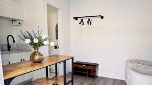 Una cocina moderna con una mesa de comedor de madera, dos taburetes, un jarrón de flores y un felpudo que dice 'WELCOME' en la entrada.