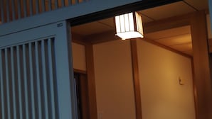 Sisätilojen käytävä, jossa on puulattia, perinteinen liukuovi ja katosta roikkuva valaisin.