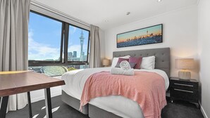 Habitación de hotel con una cama grande, un escritorio, vista a la ciudad y un cuadro en la pared.