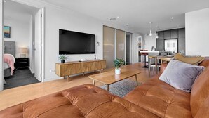 Una sala de estar moderna con un televisor de pantalla plana grande, una mesa de centro de madera y un sofá de cuero marrón.