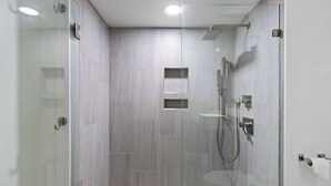 A modern shower area with a glass door, a handheld showerhead, and a wall-mounted control panel.