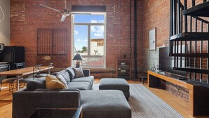 A modern living room with a brick wall, a large window, a sofa, a TV, and a wooden bench.
