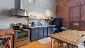 A modern kitchen with stainless steel appliances, a wooden table, and a brick wall.
