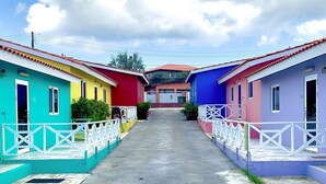 Une rangée de maisons colorées avec des balustrades blanches, un chemin central et, au fond, un bâtiment avec un toit rouge.