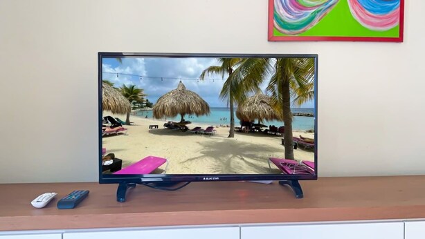 Un téléviseur diffusant une scène de plage avec des palmiers et des chaises longues.