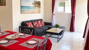 Un coin repas avec une table dressée pour deux personnes, un canapé, une table basse et un tableau représentant une scène de plage.