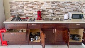 Une cuisine compacte avec un plan de travail carrelé, une cuisinière à gaz, une cafetière rouge, un four à micro-ondes et un évier.